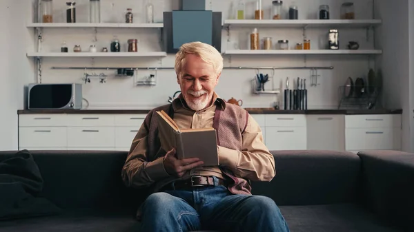 Счастливый пожилой человек, читающий книгу дома — стоковое фото