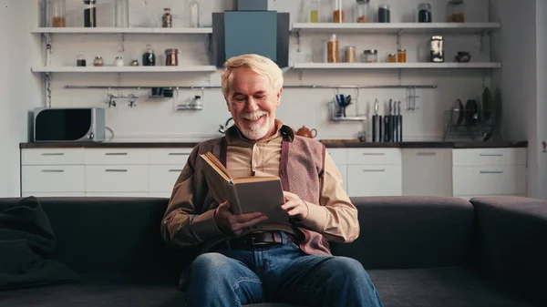 Sonriendo hombre mayor leyendo libro en casa - foto de stock