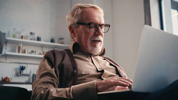 Uomo anziano in occhiali da vista utilizzando il computer portatile a casa — Foto stock