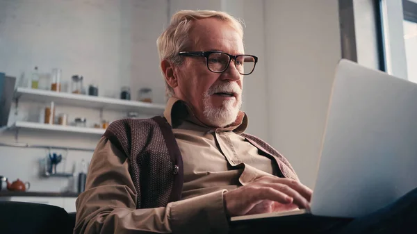 Uomo in pensione in occhiali da vista utilizzando il computer portatile a casa — Foto stock