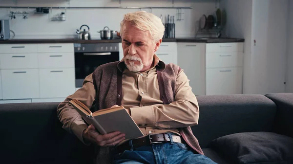 Зосереджений старший чоловік читає книгу вдома — стокове фото