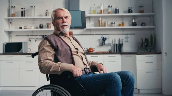 Инвалид-пенсионер смотрит в камеру, сидя в инвалидном кресле — стоковое фото