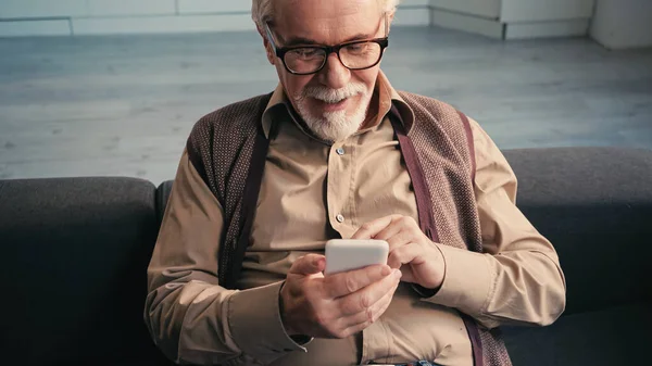 Glücklicher Rentner mit Brille, der auf dem Smartphone SMS schreibt — Stockfoto