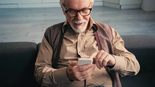 Homme retraité joyeux dans les lunettes textos sur smartphone — Photo de stock