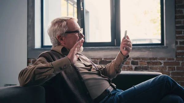 Bärtiger Rentner mit Brille winkt bei Videoanruf auf Smartphone — Stockfoto