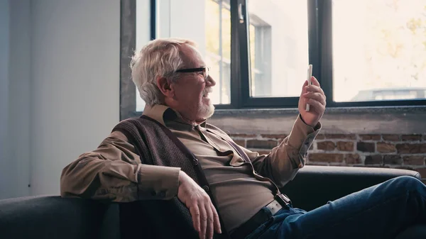 Side view of happy pensioner in eyeglasses having video call on smartphone — Stock Photo