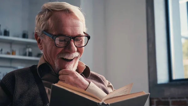 Happy senior man in eyeglasses reading book at home — Stock Photo