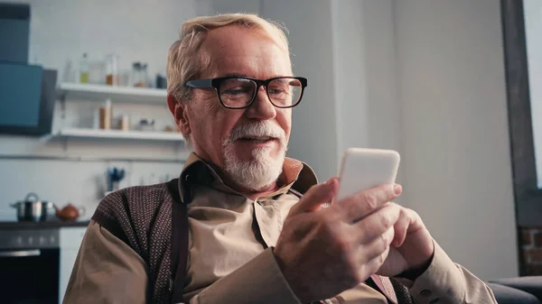 Positive pensioner in eyeglasses using mobile phone — Stock Photo