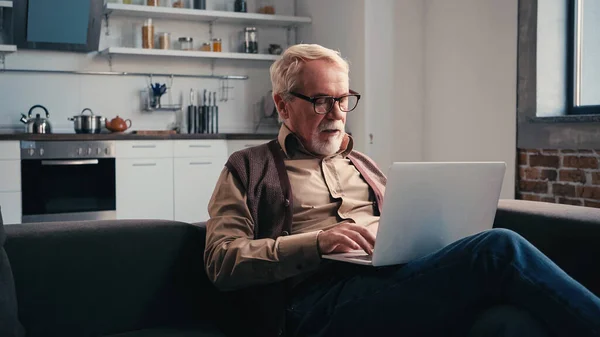 Senior freelancer in eyeglasses using laptop at home — Stock Photo