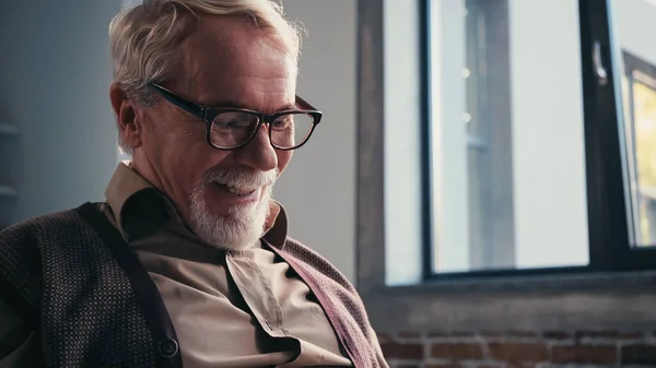 Cheerful and beaded retired man in eyeglasses looking down — Stock Photo