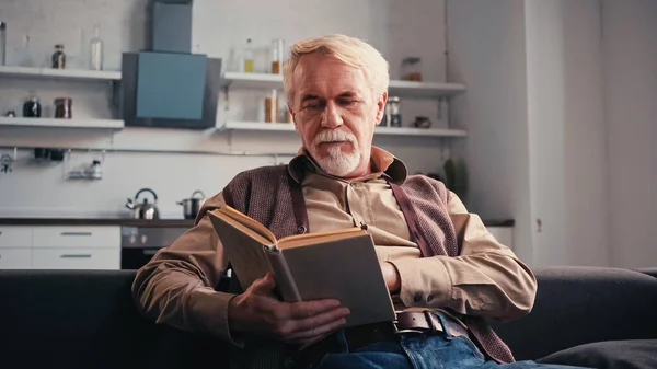 Barbudo aposentado homem leitura livro em casa — Fotografia de Stock