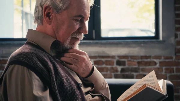 Homem aposentado barbudo lendo romance em casa — Fotografia de Stock