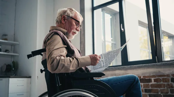 Handicapped senior man in wheelchair reading newspaper — Stock Photo