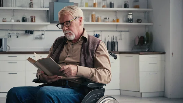 Discapacitado hombre mayor en silla de ruedas lectura novela - foto de stock