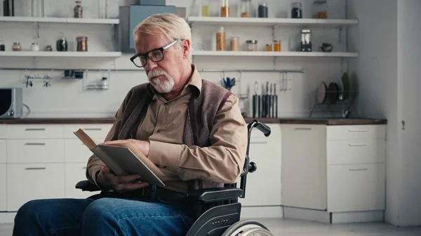 Hombre mayor discapacitado en silla de ruedas lectura novela - foto de stock