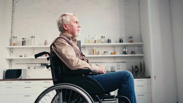 Vista lateral do homem barbudo aposentado em cadeira de rodas olhando para longe em casa — Fotografia de Stock