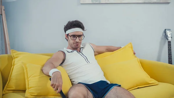 Ленивый мужчина в спортивной одежде смотрит телевизор, сидя на диване в гостиной — стоковое фото