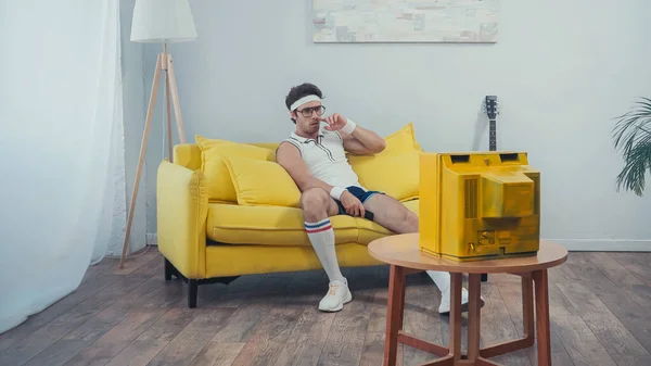 Fauler Mann in Sportbekleidung, der sich auf dem Sofa im Wohnzimmer die Nase zuhält — Stockfoto