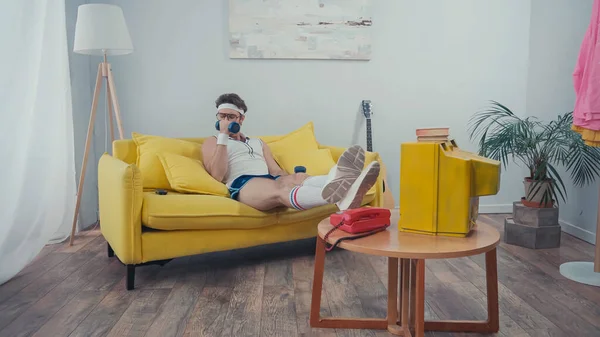 Sportsman training with dumbbells while sitting on couch near retro tv in living room — Stock Photo