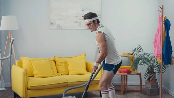 Sportsman vacuum cleaning living room, retro sport concept — Stock Photo