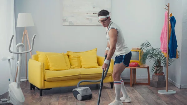 Young man in sportswear vacuum cleaning living room, retro sport concept — Stock Photo