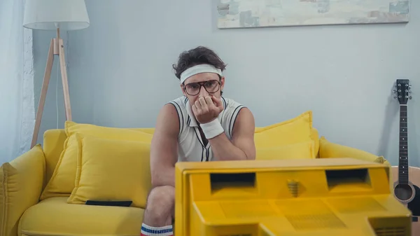 Hombre aburrido en ropa deportiva retro sentado en el sofá y viendo la televisión — Stock Photo