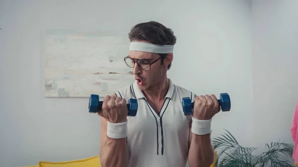 Mann in Retro-Sportbekleidung und Brille hebt daheim Hanteln — Stockfoto