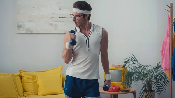 Funny sportsman in eyeglasses lifting weight in living room, retro sport concept — Stock Photo