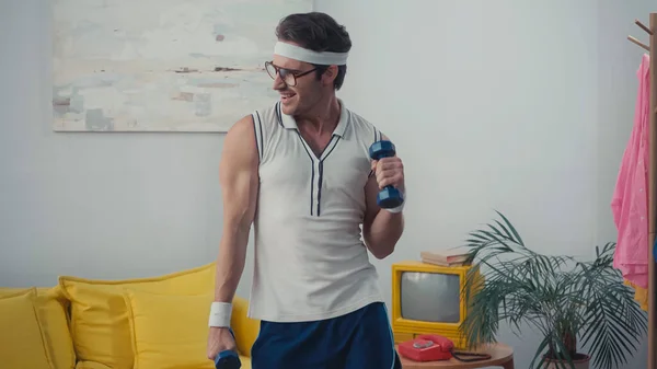 Funny sportsman exercising with dumbbells in living room, retro sport concept — Stock Photo