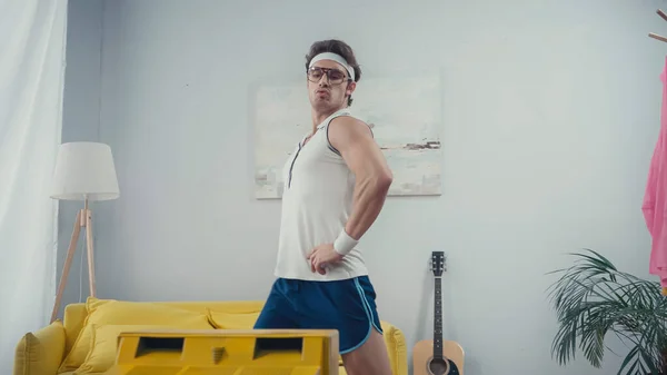 Funny sportsman with hands on hips doing lunges in front of retro tv at home — Stock Photo