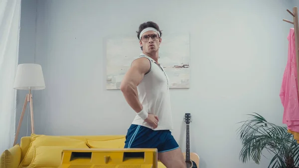 Young sportsman with hands on hips doing lunges in front of retro tv at home — Stock Photo