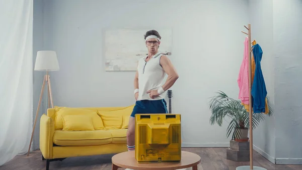 Funny sportsman with hands on hips exercising in front of retro tv at home — Stock Photo