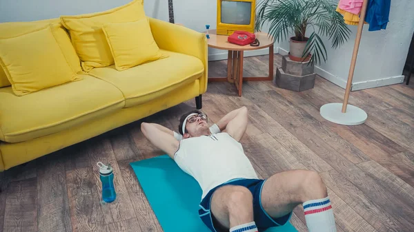 Deportista haciendo abdominales en la alfombra de fitness en la sala de estar, concepto de deporte retro - foto de stock