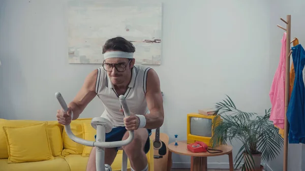 Entraînement sportif concentré sur vélo d'appartement dans le salon, concept sportif rétro — Photo de stock