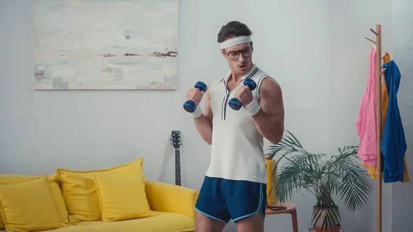 Young sportsman working out with dumbbells in living room, retro sport concept — Stock Photo