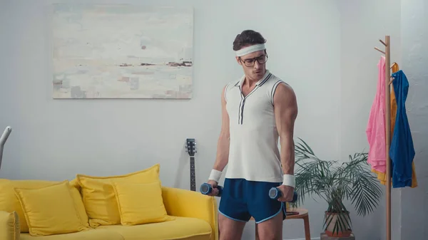 Fuerte deportista haciendo ejercicio con pesas en la sala de estar, concepto de deporte retro - foto de stock