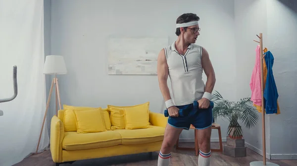 Deportista divertido haciendo ejercicio con pesas en la sala de estar, concepto de deporte retro - foto de stock