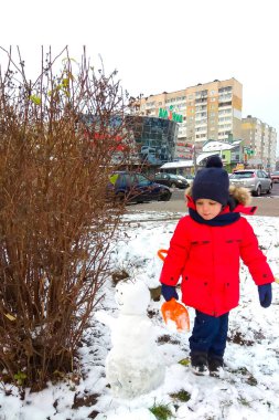 Bir çocuk şehir avlusunda kardan adam yapıyor. Elinde bir omuz bıçağı var. O, kışlık kırmızı bir ceket, mavi bir şapka, pantolon, eldivenler ve botlar giyiyor. Kardan adam gözleri yapraktan yapılır, saçlar ve ağız dallardan yapılır. Çok fazla kar var..