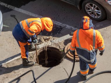 Sokaktaki açık kanalizasyon kapağının üstündeki işçiler. Kanalizasyon, yeraltı tesisleri, su tedarik sistemi, su borusu kazası.