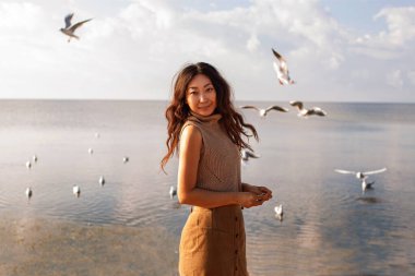 Güzel Asyalı Kadın Deniz kenarında martılarla poz veriyor.