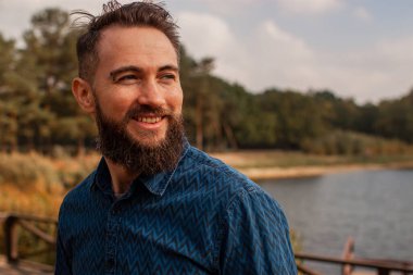 Genç sakallı adam sonbahar parkında kahve içiyor.