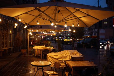 Geceleri bir kafede şemsiyeli ve çelenkli masalar.
