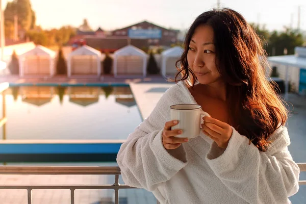 Asian Woman In Hotel Room Poolside Drinking Coffee on the balcony