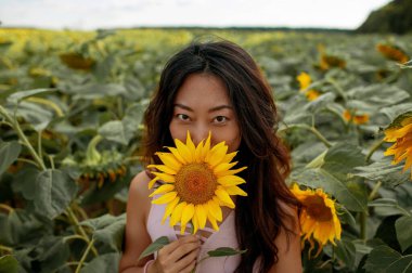 Güzel Asyalı kadın tarımsal alanda ayçiçeğiyle poz veriyor. 