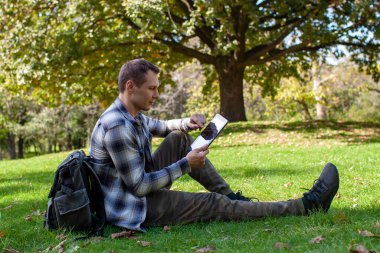 Parkta çayırda otururken dizüstü bilgisayarında yazan mutlu erkek öğrenci.