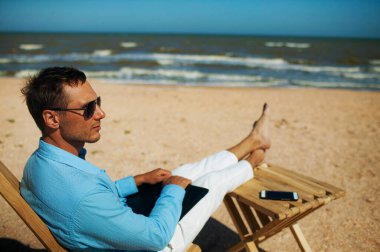 Plaj tatili sırasında dizüstü bilgisayarı olan genç bir adam.