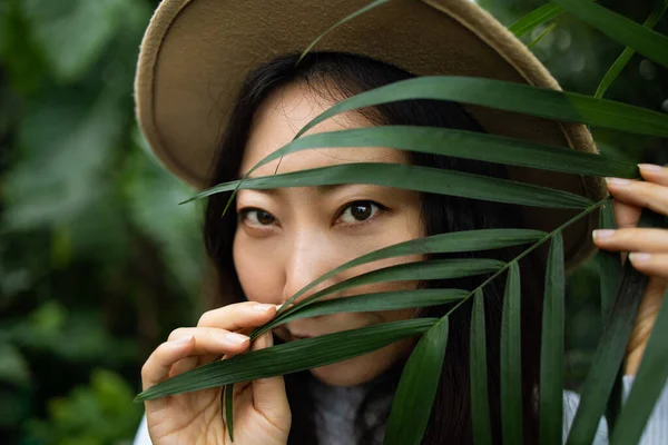Portrait Of A Young Asian Beautiful Woman Behind A Tropical Leaf And Looking At Camera.