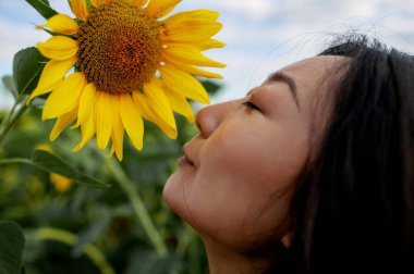 Güzel Asyalı kadın tarımsal alanda ayçiçeğiyle poz veriyor. 