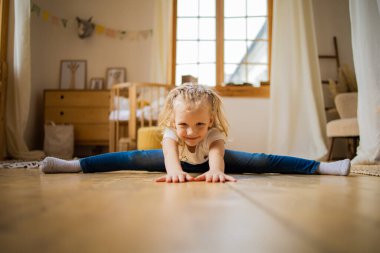 Tahta zeminde, enine bir ipin üzerinde oturan kız çocuğu.