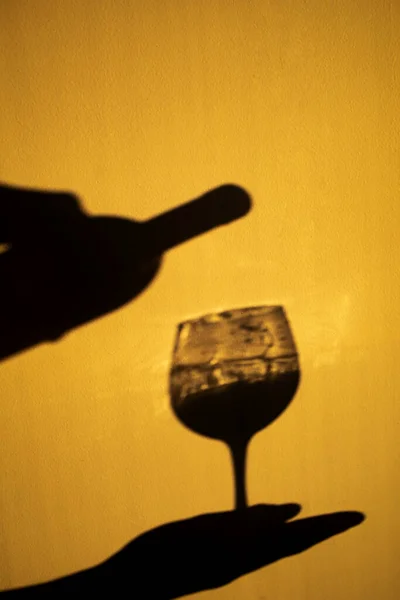 Person Shadow Holding A Wine Glass On Yellow Wall. Shadow Of man Drinking Wine